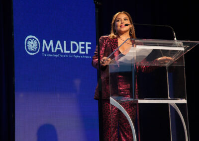 Justina Machado in a pink leopard print suit standing at a podium for the MALDEF Los Angeles Gala, 2019
